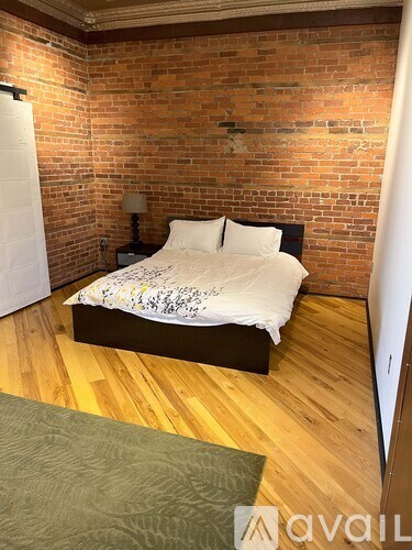 A bedroom with a brick wall and a bed with a white comforter.