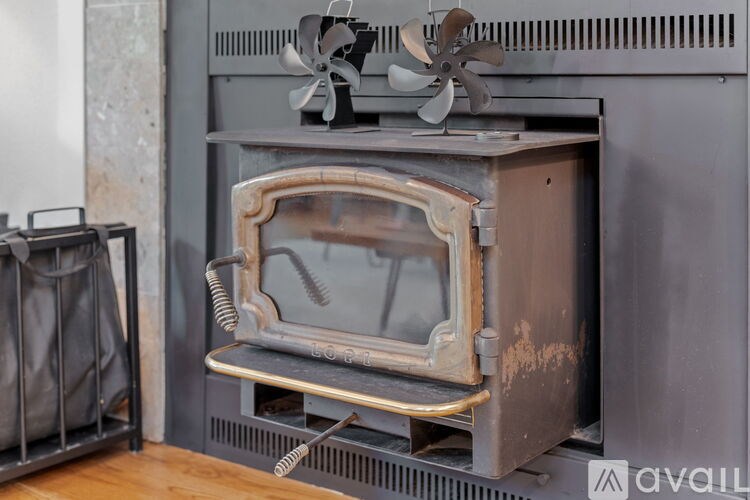 A black wood stove with a fan on top and a metal grate in front.