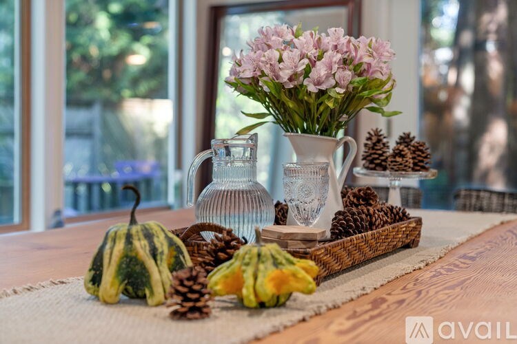 A table with a vase of flowers, a pitcher, and a basket of pinecones.