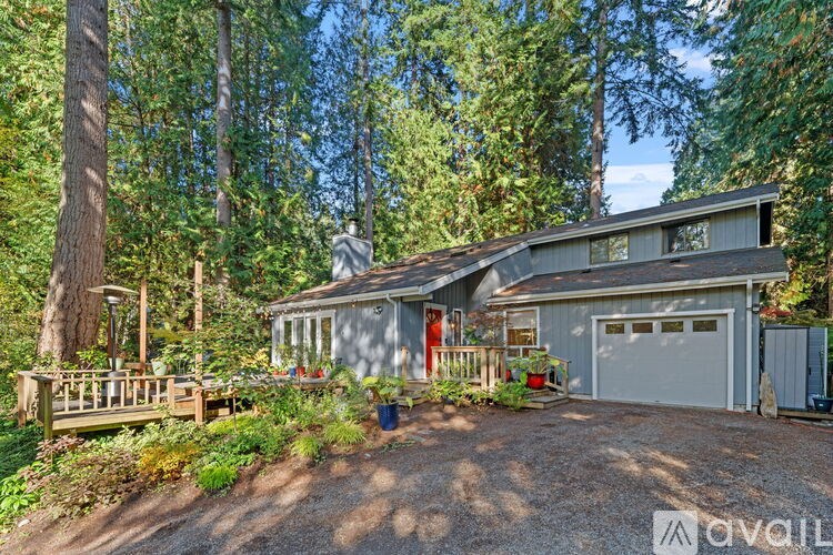 A house with a garage is surrounded by trees and has a gravel driveway.