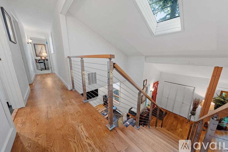 A wooden staircase with a metal railing leads to a loft area with a skylight.