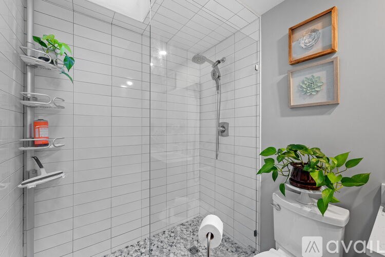 A bathroom with a white tiled shower and a toilet with a plant on top.