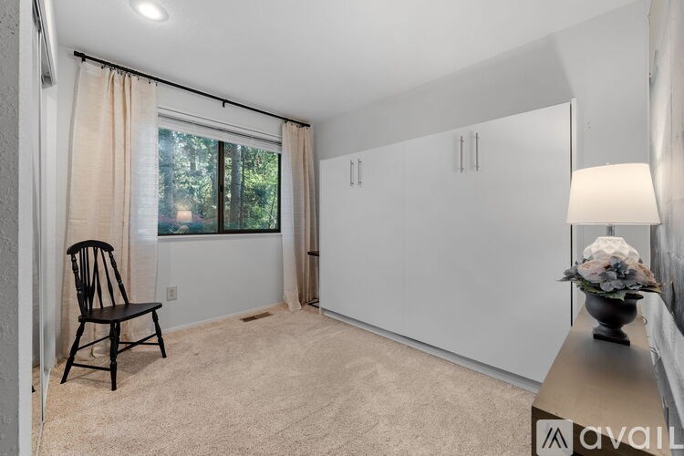 A room with a chair, a table with a vase, and a window with curtains.