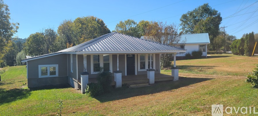 A house with a porch and a covered patio is surrounded by a grassy yard.