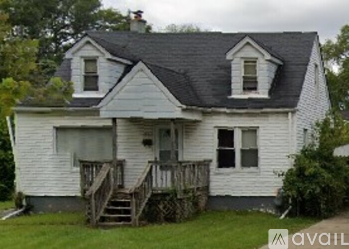 A white house with a black roof and a wooden staircase leading to the door.