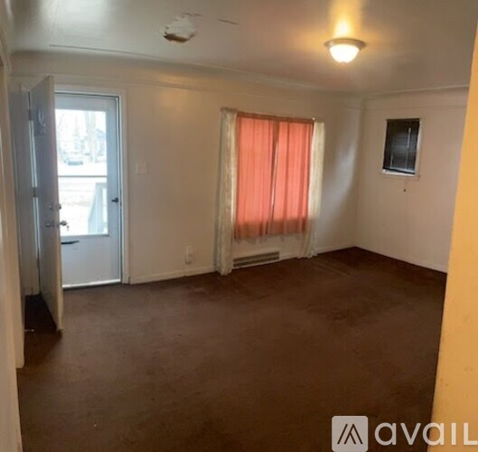 A room with a window covered by orange curtains and a small window on the wall.