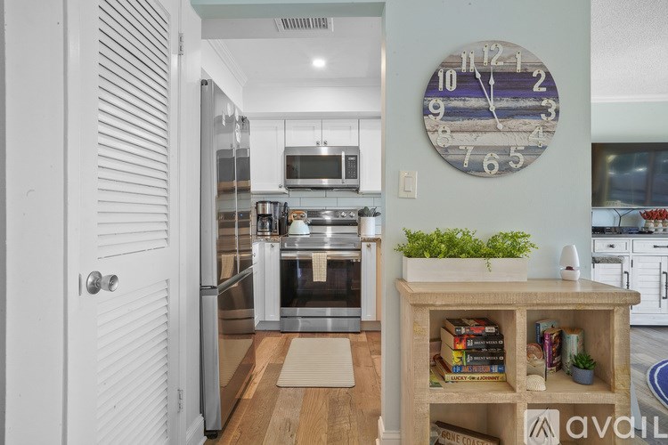 A kitchen with a clock on the wall and a bookshelf with books and plants.