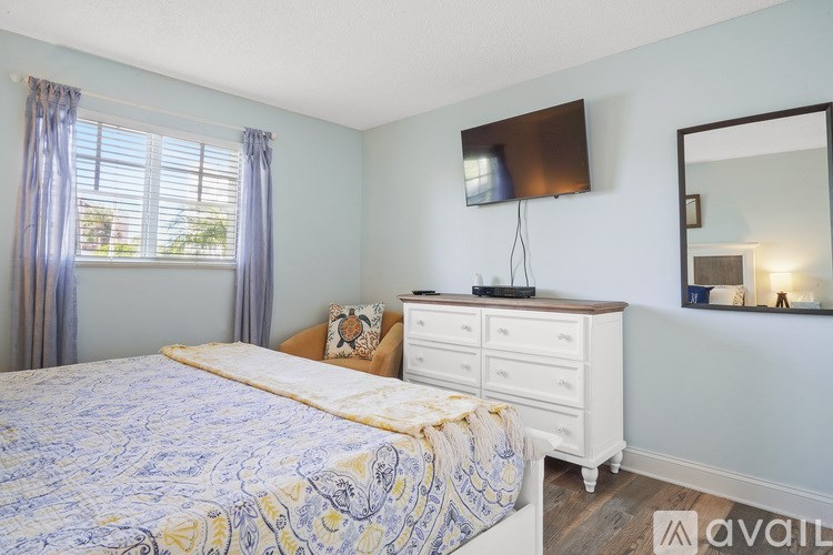 A bedroom with a bed, dresser, mirror, and window with curtains.