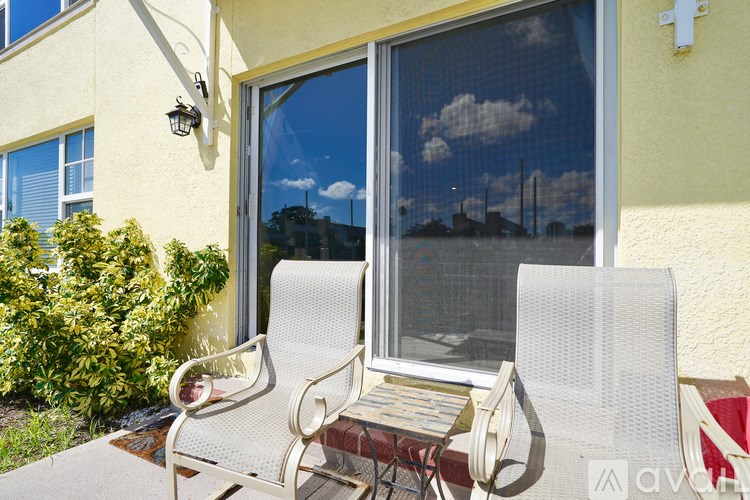 Two white chairs are placed on a patio in front of a window.