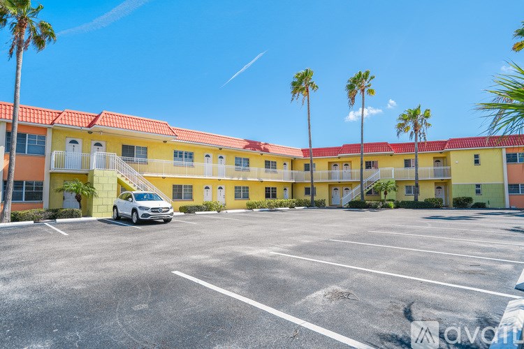 A white car is parked in a parking lot in front of a yellow building with palm trees.