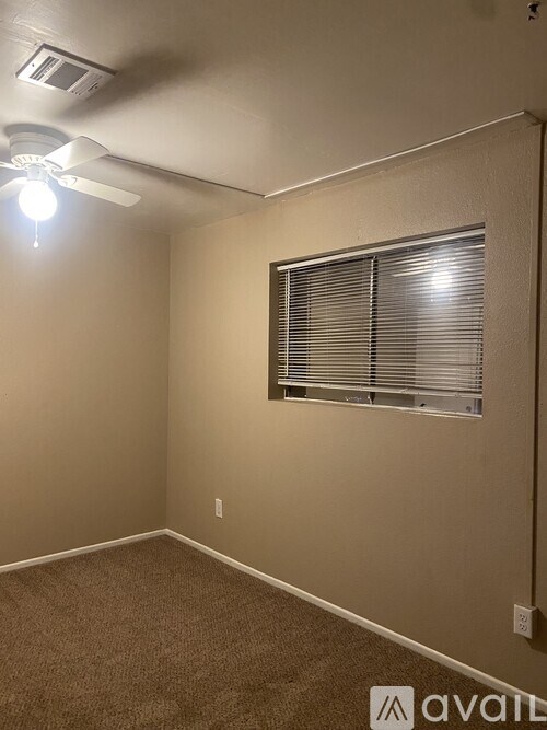 A room with a carpeted floor, a ceiling fan, and a window with blinds.