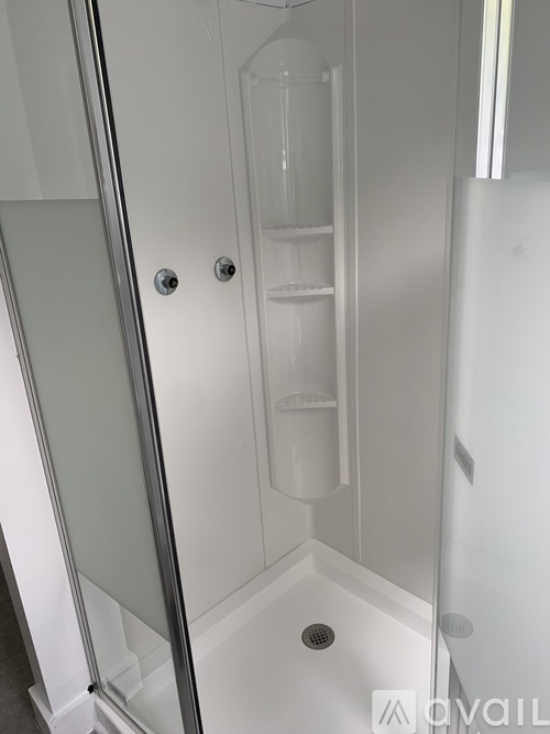 A white shower stall with a glass door and a drain in the bottom.