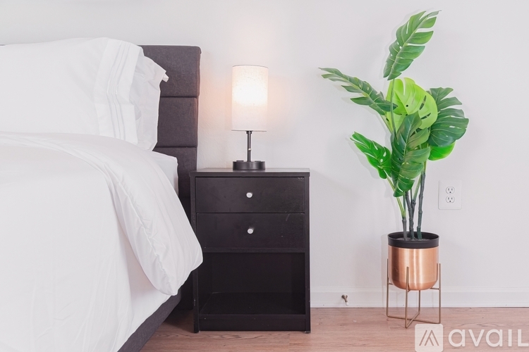 A bedroom with a bed, a nightstand with a lamp, and a plant.