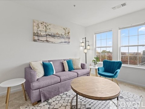 A living room with a purple couch, a blue chair, and a painting on the wall.
