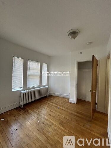 A room with wooden floors and white walls, with a window and a radiator.