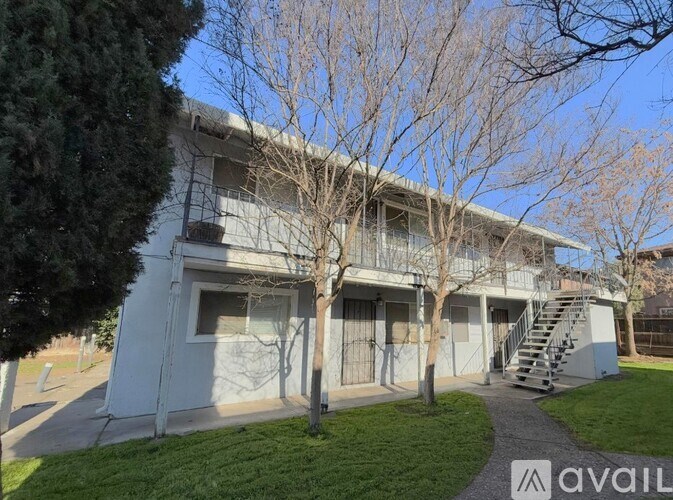 A white building with a balcony and a staircase is surrounded by trees and grass.