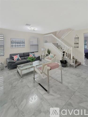 A living room with a grey sofa, a glass coffee table, and a staircase.