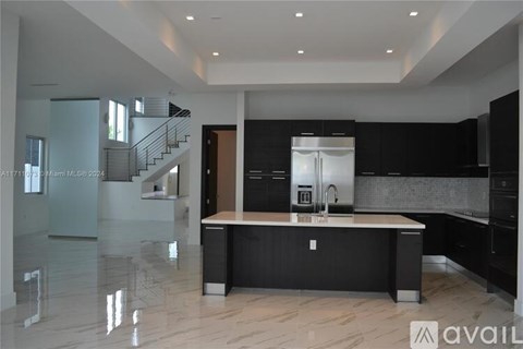 A modern kitchen with a central island and a staircase in the background.