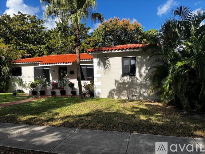 A house with a red tile roof and a white exterior is surrounded by greenery.
