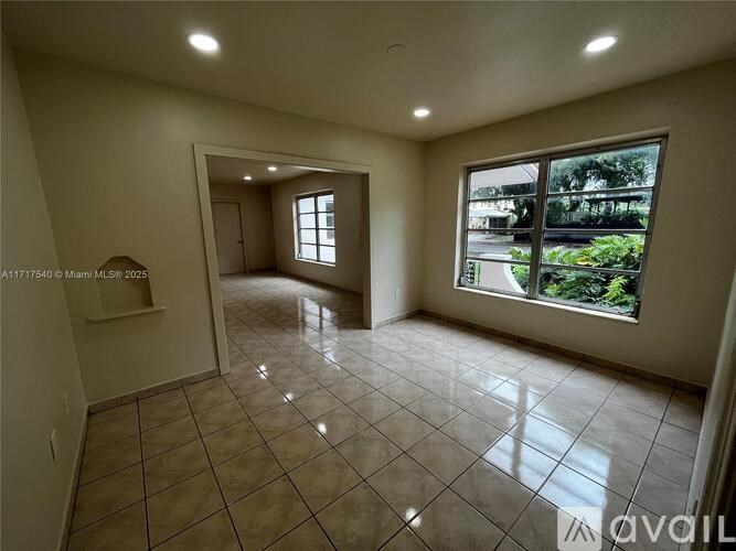 A spacious room with tiled flooring and a large window overlooking a green area.