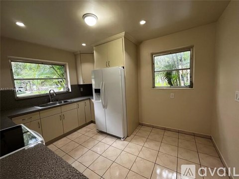 A kitchen with a white refrigerator and a window with a view of trees.