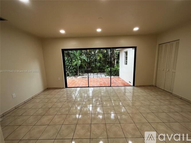 A spacious room with tiled flooring and a view of a garden through a glass door.