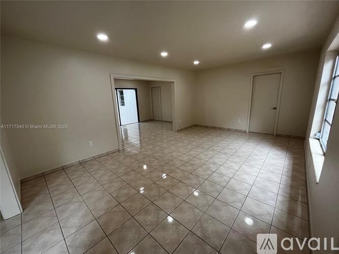 A spacious room with tile flooring and a large window on the right side.