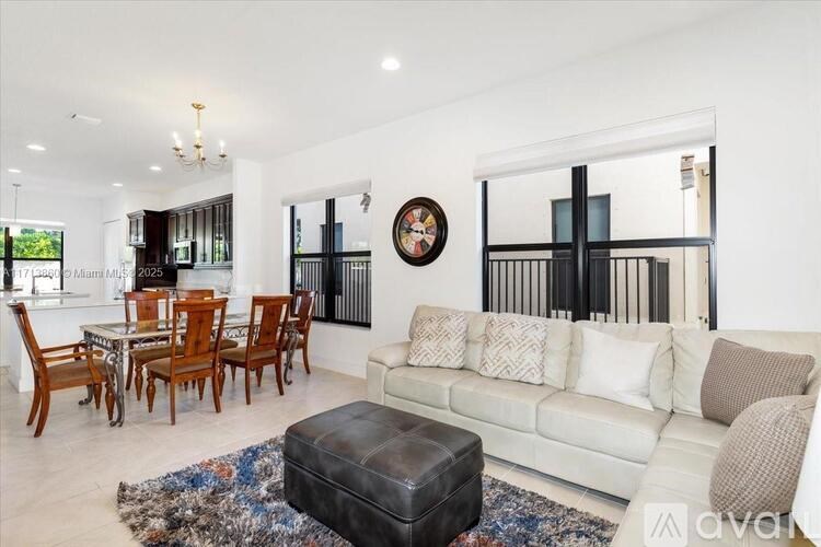 A living room with a white couch, wooden chairs, and a large clock on the wall.