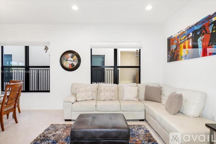 A living room with a white couch, a brown leather ottoman, and a large painting on the wall.