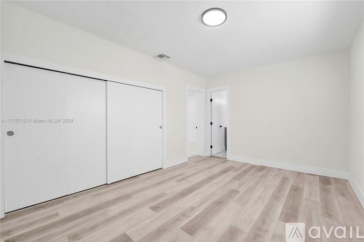 A room with white walls and a wooden floor with a white door on the right side.