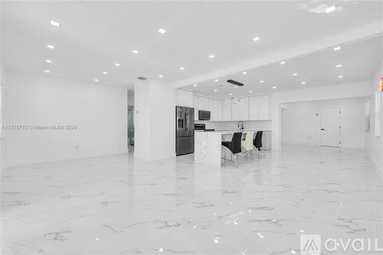 A spacious white room with marble flooring and a kitchen area in the background.