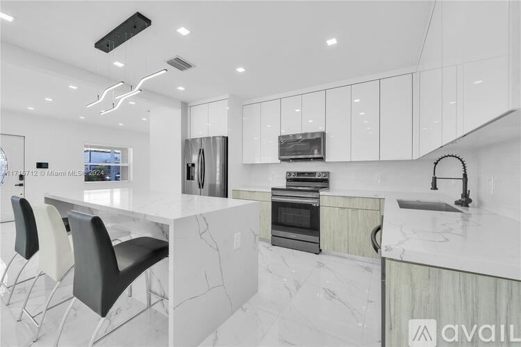 A modern kitchen with white marble countertops and black chairs.