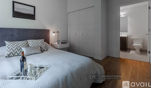 A bedroom with a bed, nightstand, and a tray with a bottle and glasses on it.