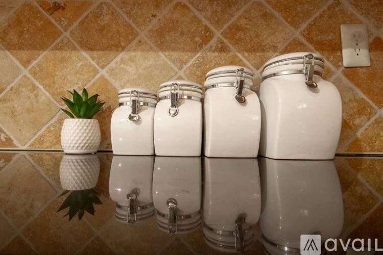Four white ceramic jars with metal clasps are lined up on a tiled surface.