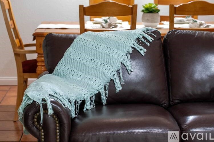 A blue knitted throw is draped over a brown leather couch.