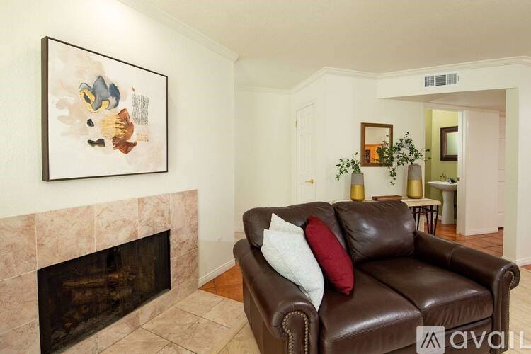 A brown leather couch with a red pillow is in front of a fireplace.