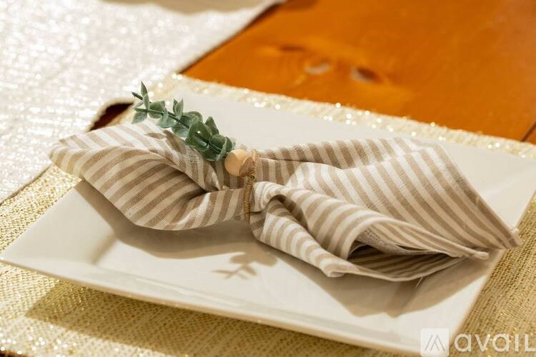 A white plate with a napkin folded into a bow and a sprig of greenery on top.