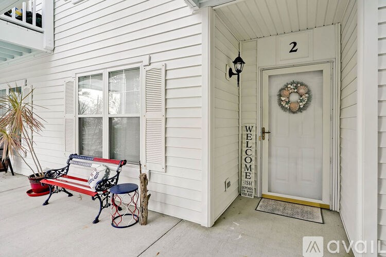 A white house with a wreath on the door and a bench with an American flag on it.