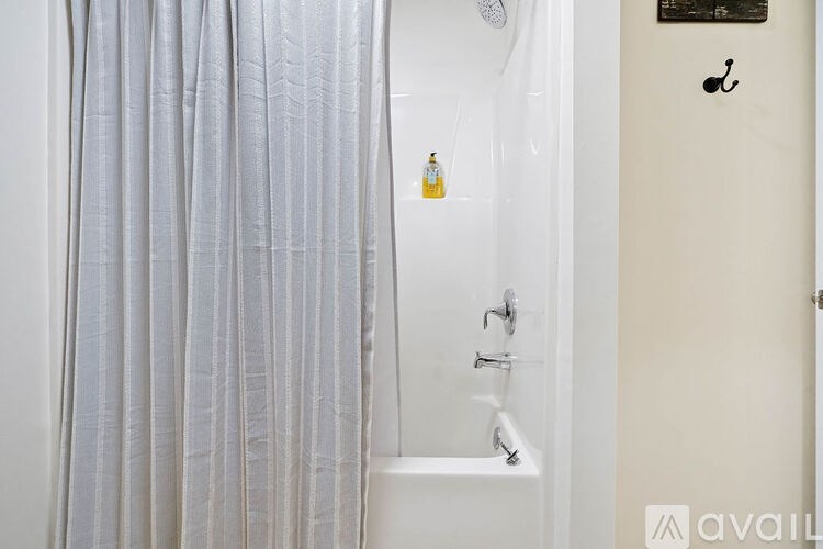 A bathroom with a white tub and grey curtains.