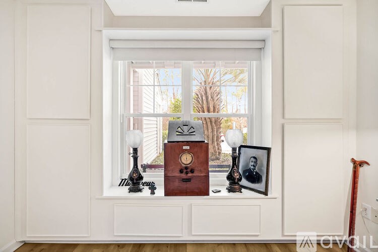 A room with a window, a lamp, a clock, a picture frame, and a cane.