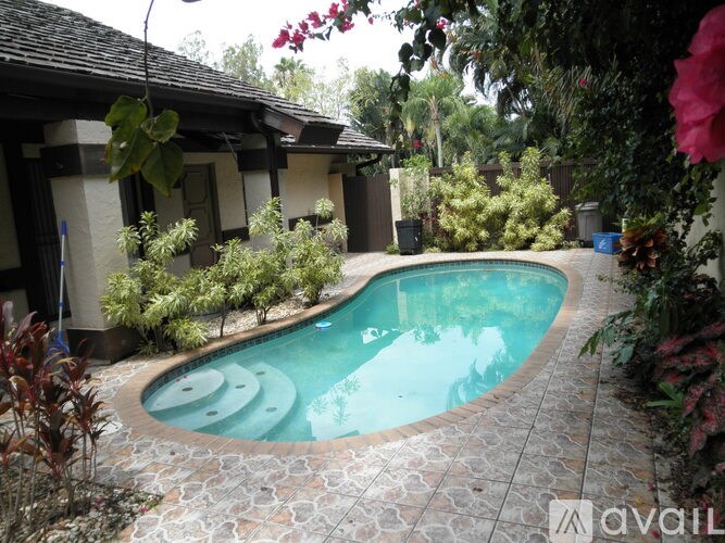 A small pool surrounded by plants and a house.