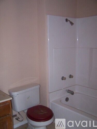 A white toilet with a red seat sits next to a white bathtub in a bathroom.