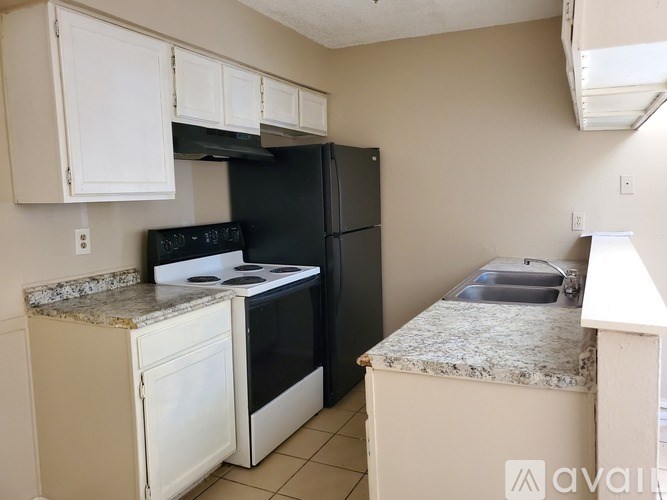 A kitchen with a black refrigerator, white cabinets, and a granite countertop.