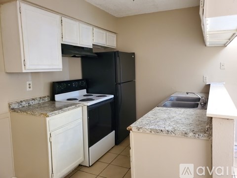 A kitchen with a black refrigerator, white cabinets, and a granite countertop.