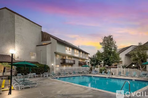 A pool area with chairs and umbrellas in front of a building.