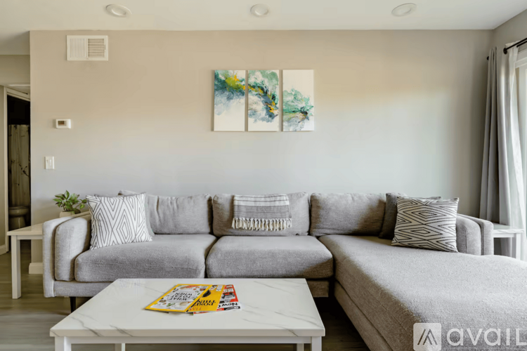 A living room with a grey couch and a painting on the wall.