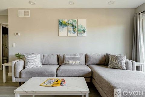 A living room with a grey couch and a painting on the wall.