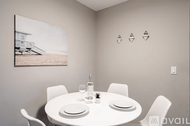 A dining room with a white table set for two and a picture of a beach house on the wall.