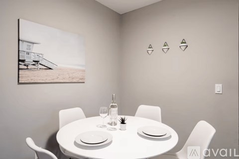 A dining room with a white table set for two and a picture of a beach house on the wall.