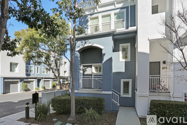 A tree stands in front of a blue building with a white balcony.